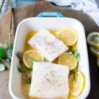 The seasoned halibut fish fillets are placed on top of the lemon garlic herb and butter layer on the baking dish