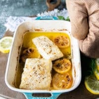 The halibut fish is out of the oven and a hand is holding the dish showing the succulent cooked halibut recipe