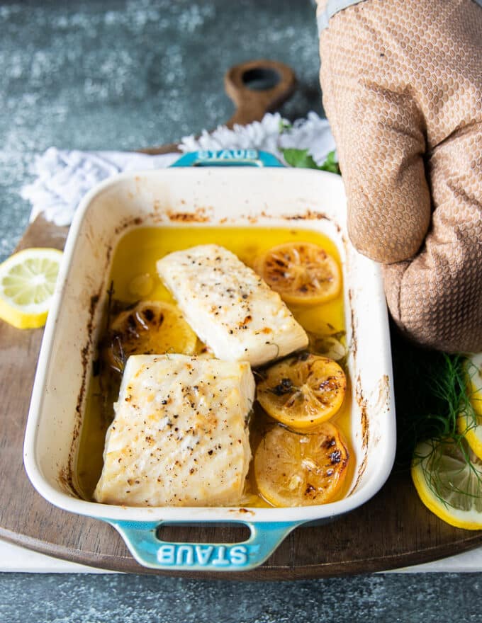 The halibut fish is out of the oven and a hand is holding the dish showing the succulent cooked halibut recipe