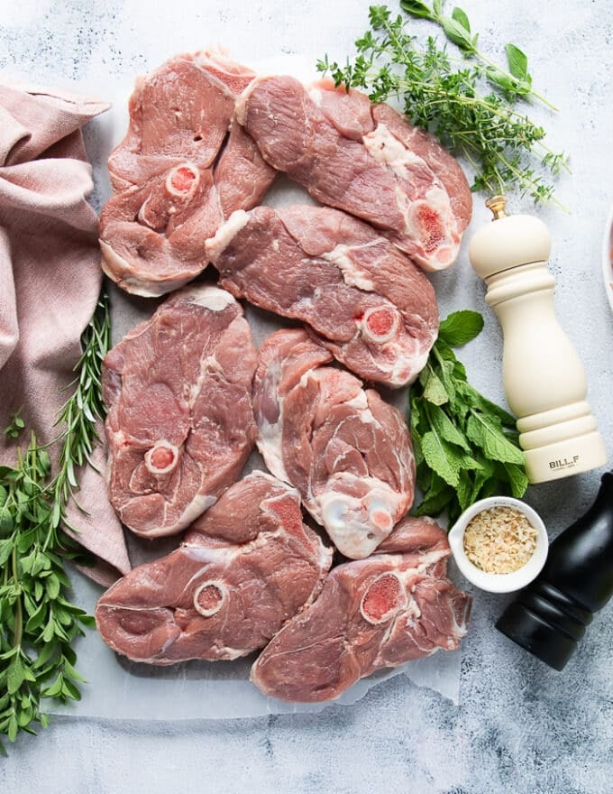 Ingredients to make lamb steaks including the leg of lamb cut into steaks, salt, pepper, onion flakes and herb butter