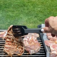 a hand flipping a grilled steak on the charcoal grill to show the grill marks