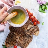 A hand pouring the herb butter over the grilled steaks