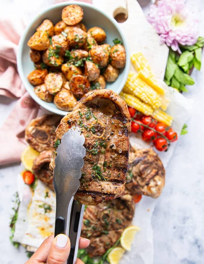 A tong showing close up of a grilled lamb steak drizzled with herb butter