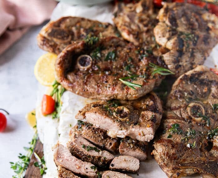 grilled lamb steaks on a platter with on steak sliced into strips to show the inside of the steak