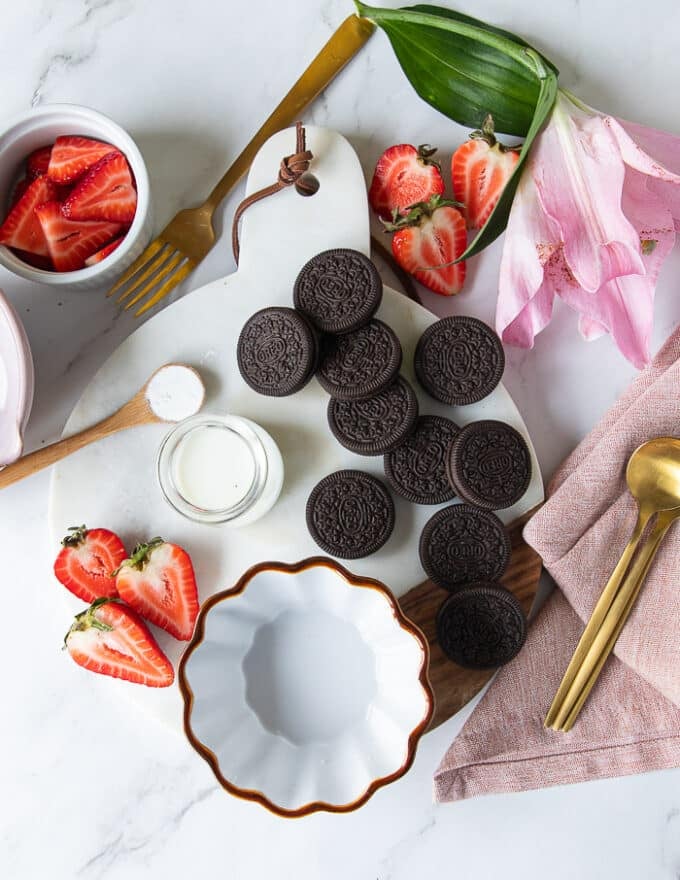 Ingredients for oreo mug cake including: oreos, milk and baking powder on a white marble surrounded by sliced strawberries