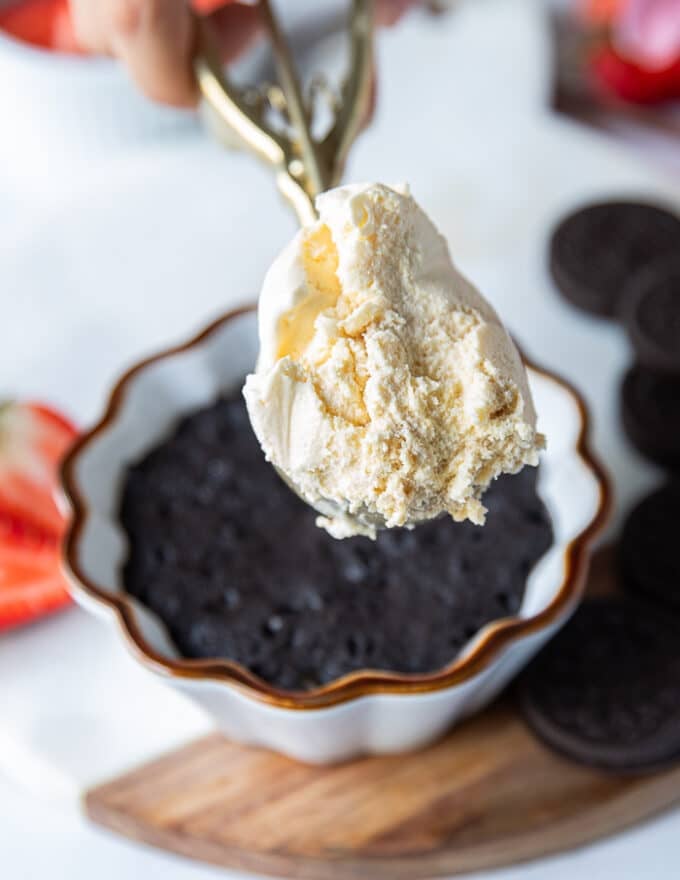 A hand holding a scoop of ice cream ready to serve over the oreo mug cake