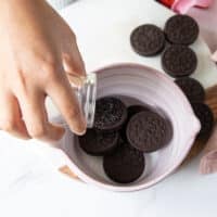 A hand pouring the milk over the oreos in to the bowl