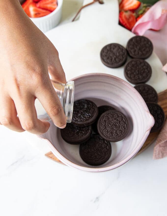 A hand pouring the milk over the oreos in to the bowl 
