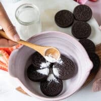 A hand pouring the baking powder over the oreo and milk in a a bowl
