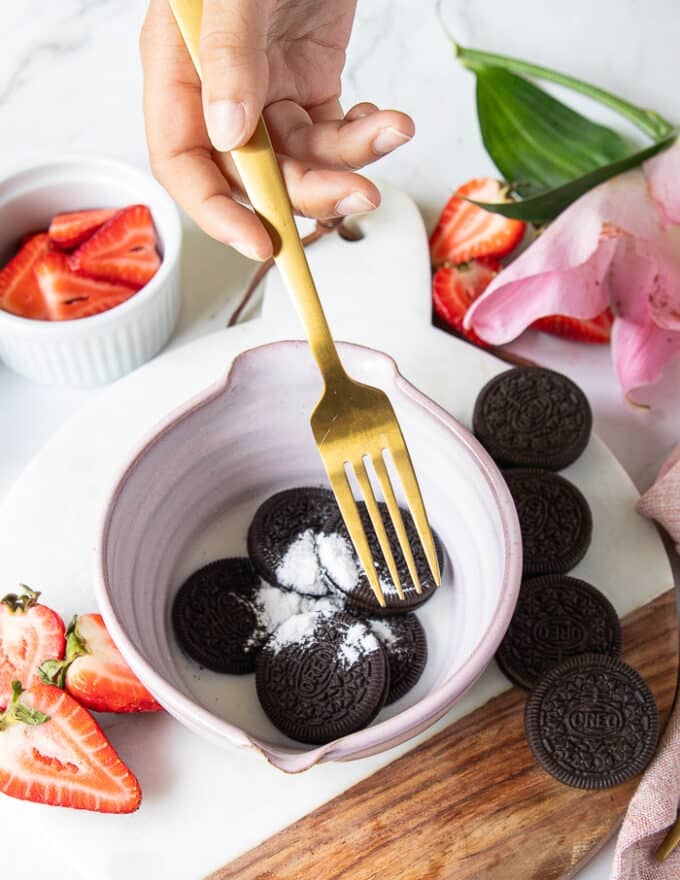 A hand holding a fork to start mashing the oreos with the ingredients to make oreo cake