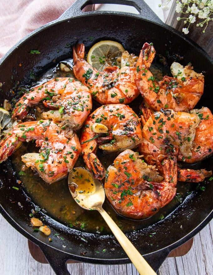 Shrimp scampi in a pan bathing in lemon garlic butter sauce and a spoon showing the scampi sauce 