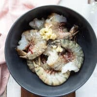 Shrimp added in a bowl with minced garlic, seasoning and fresh herbs and olive oil
