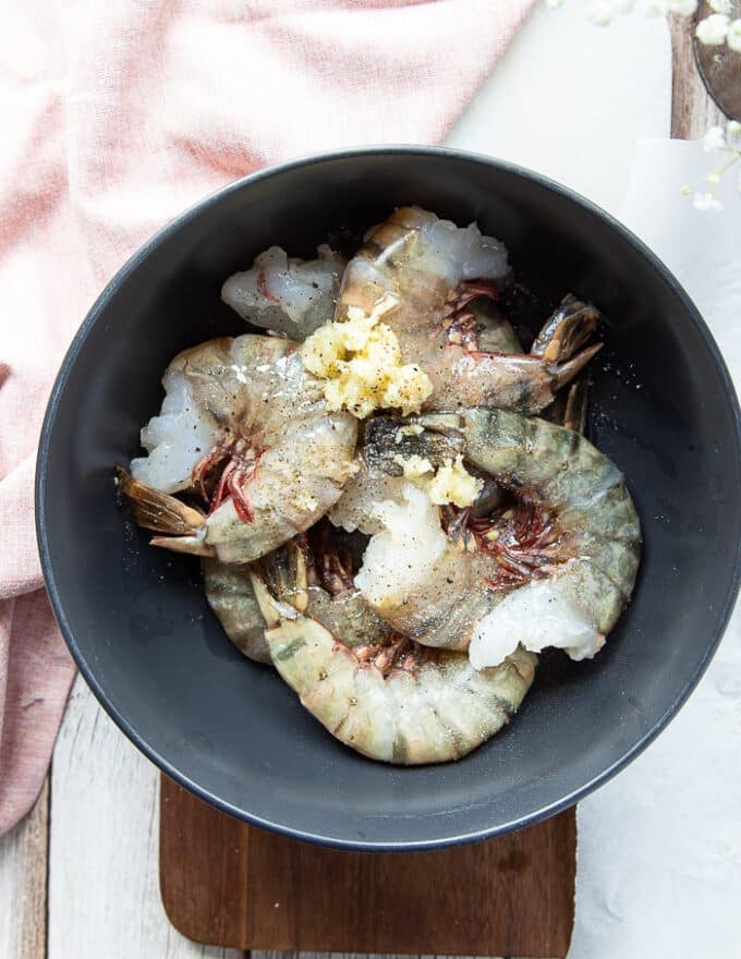 Shrimp added in a bowl with minced garlic, seasoning and fresh herbs and olive oil