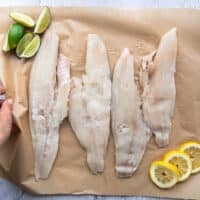 4 haddock fillets on a parchment paper surrounded by a bowl with coating ingredients