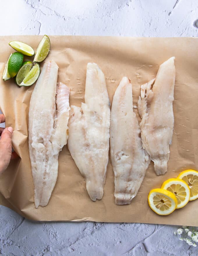 4 haddock fillets on a parchment paper surrounded by a bowl with coating ingredients 