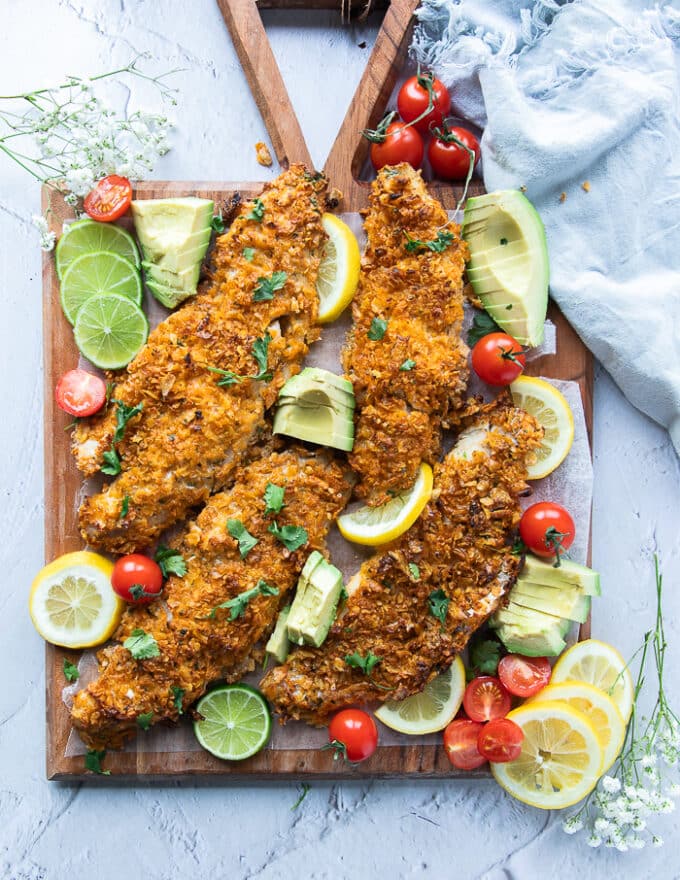 The baked haddock fillets out of the oven and placed on a large tray with avocado slices, tomatoes, lemon ad lime, and extra cilantro for garnish