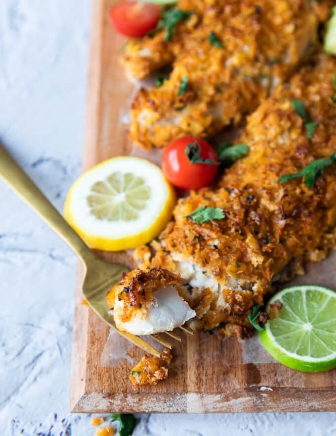 Close up of a fork holding a piece of baked haddock showing the texture of the crunchy coating and the succulent fish 