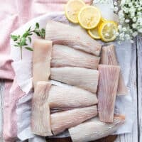 A board with fillets of mahi mahi patted dry and fresh or defrosted, surrounded by lemon slices