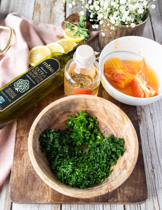 ingredients for a citrus vinaigrette in a bowl with herbs, orange juice, olive oil, vinegar 