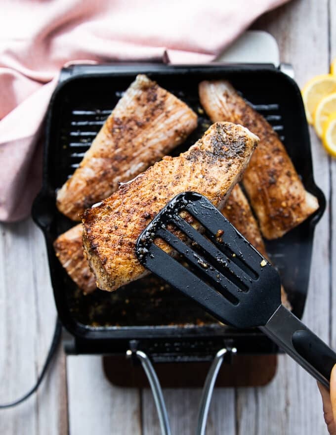 A hand showing one piece of mahi mahi fish ready to flip on the grill 