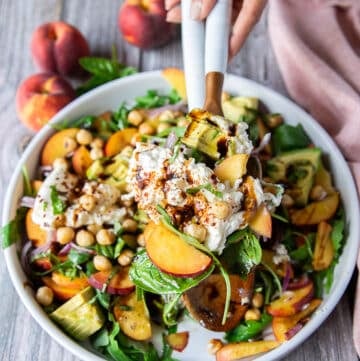 two hands serving some peach burrata salad with serving spoons showing close up of the burrata and peaches and balsamic dressing