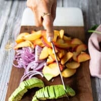 A hand slicing the fresh peaches on a cutting board to make the salad recipe