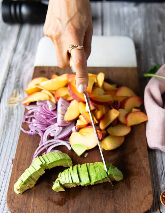 A hand slicing the fresh peaches on a cutting board to make the salad recipe