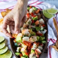 A hand holding a chip with a dip of shrimp ceviche showing close up