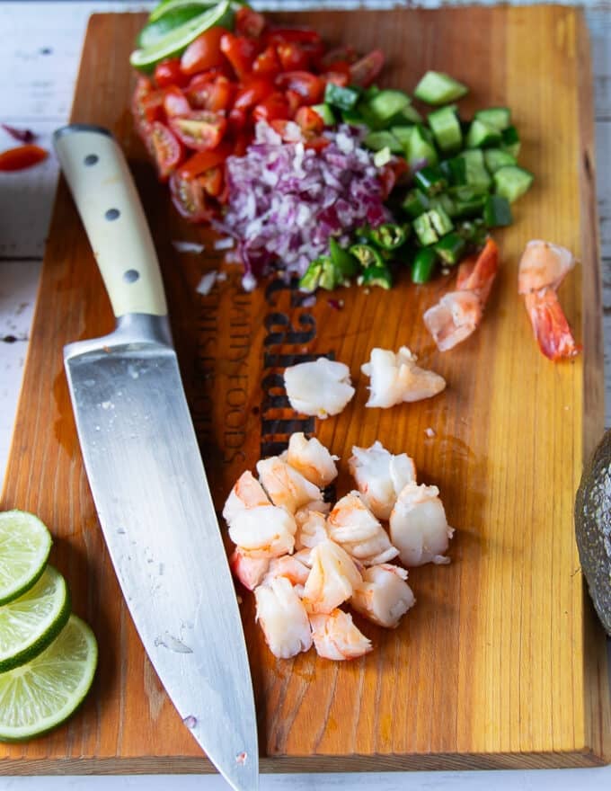 A knife dicing the shrimp on a cutting board into 1 inch pieces