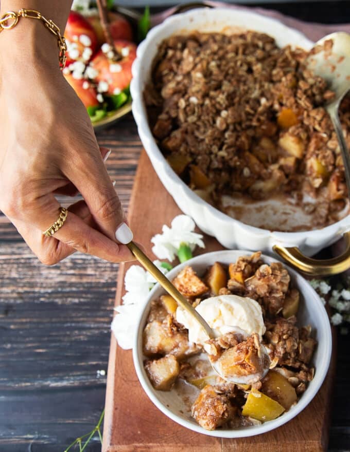 A hand holding a spoonful of apple crisp with melted vanilla ice cream over the spoon ready to eat