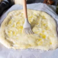 A brush is generously covering the top of the sough with olive oil and freshly cracked pepper
