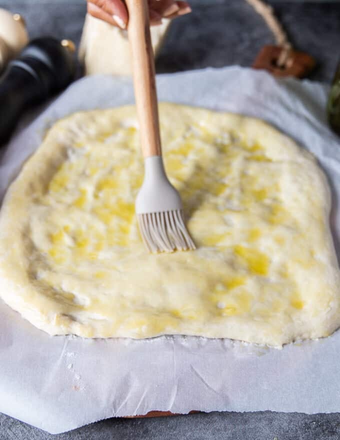 A brush is generously covering the top of the sough with olive oil and freshly cracked pepper 