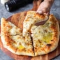 A hand holding a slice of cacio e pepe pizza showing the black pepper and pecorino cheese