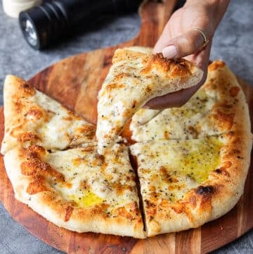 A hand holding a slice of cacio e pepe pizza showing the black pepper and pecorino cheese