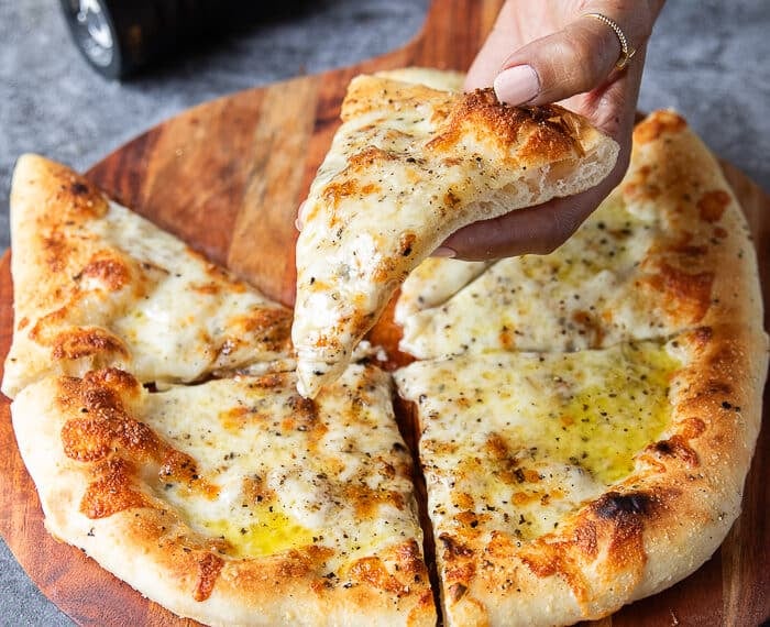 A hand holding a slice of cacio e pepe pizza showing the black pepper and pecorino cheese