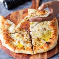 A hand holding a slice of pizza side ways showing the crust