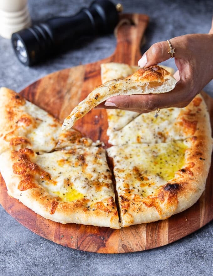 A hand holding a slice of pizza side ways showing the crust 