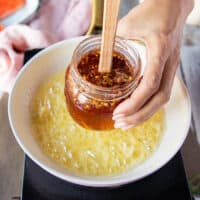 A hand holding the hot honey recipe and ready to pour it over the butter and garlic
