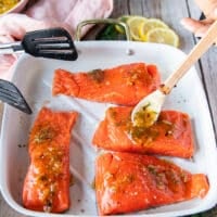 A hand pouring the glaze over the salmon before baking