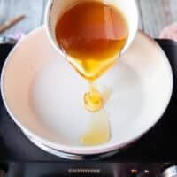 A hand pouring some honey into a sauce pan