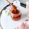 A jar of hot honey and a honey dipper showing the hot honey dripping in the jar