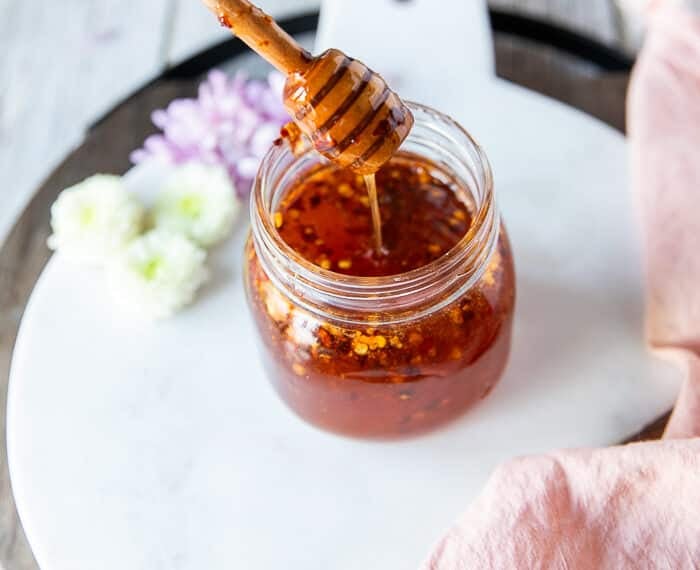 A jar of hot honey and a honey dipper showing the hot honey dripping in the jar