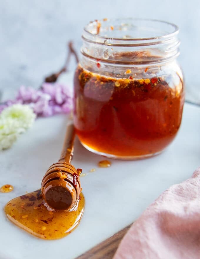A jar of hot honey on a white marble and a honey dipper on the surface with hot honey recipe over a marble showing the sauce texture