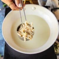 A hand holding a quarter cup measuring cup filled with potato pancake mixture portioned and ready to cook it in hot oil.