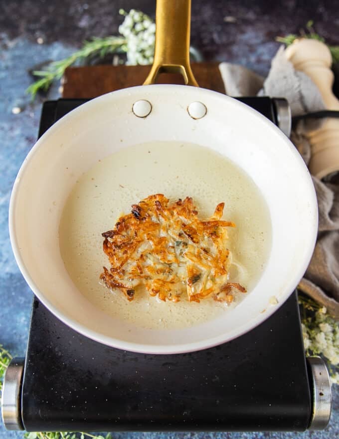 Golden potato pancakes, flipped and cooking in a hot skillet with oil 