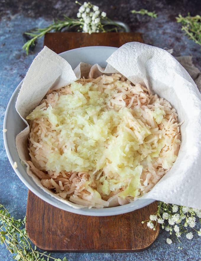 Potatoes and onions grated in a bowl lied with kitchen towel