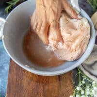 A hand squeezing out all the excess moisture from the onions and potatoes grated in the bowl