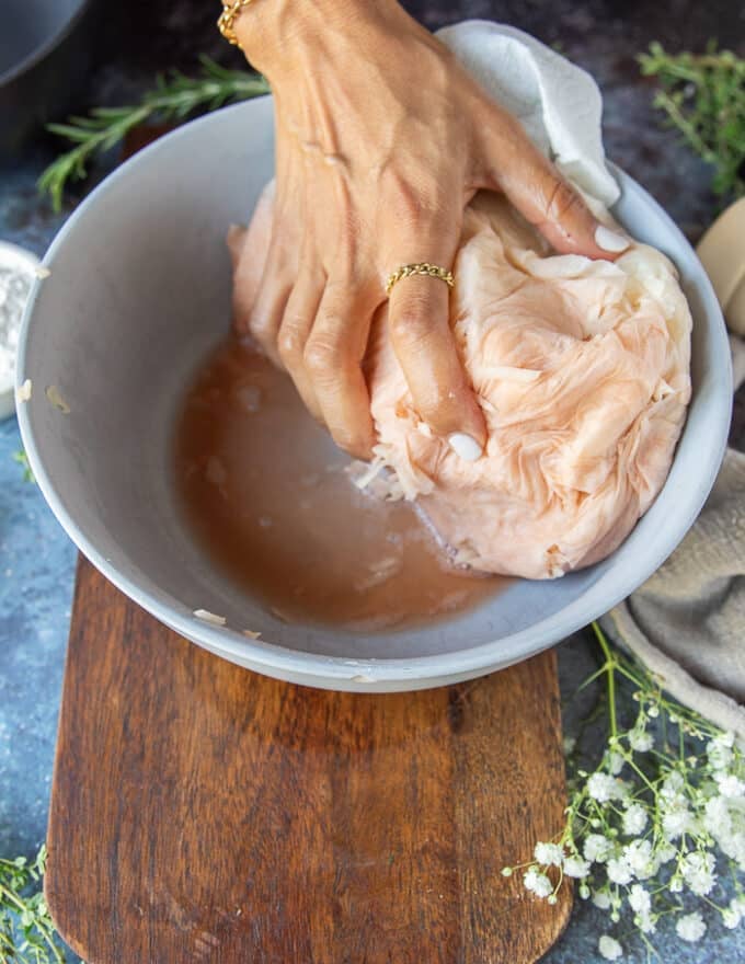 A hand squeezing out all the excess moisture from the onions and potatoes grated in the bowl 