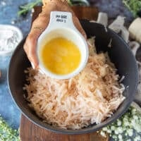 A hand holding an egg and pouring it over the squeezed potatoes and onions in a new bowl