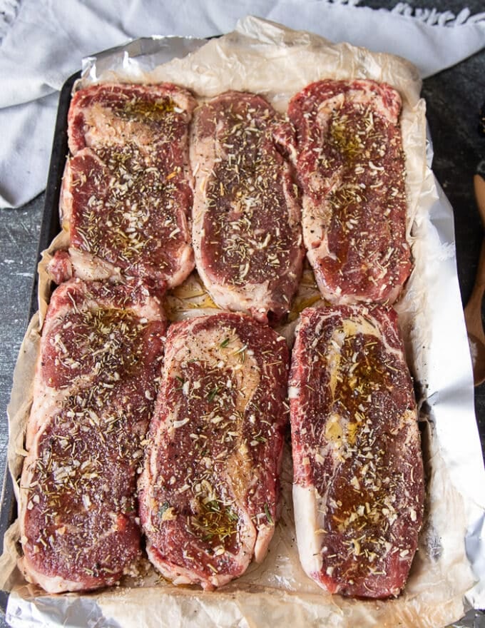 A tray of ribeye steaks seasoned on both sides and ready to cook